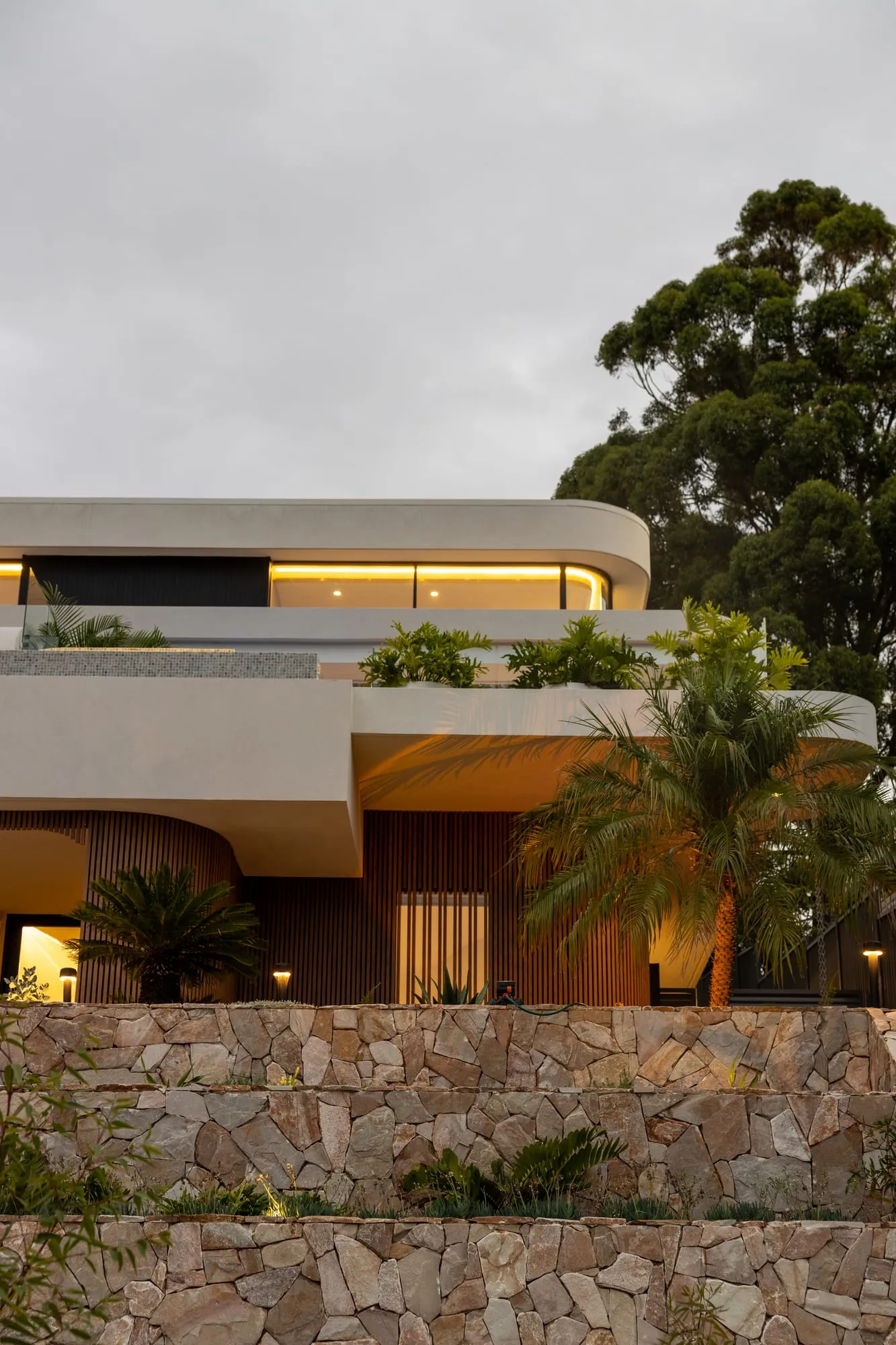 The Yowie Bay home at dusk, its curved timber-batten forms glowing against the sky