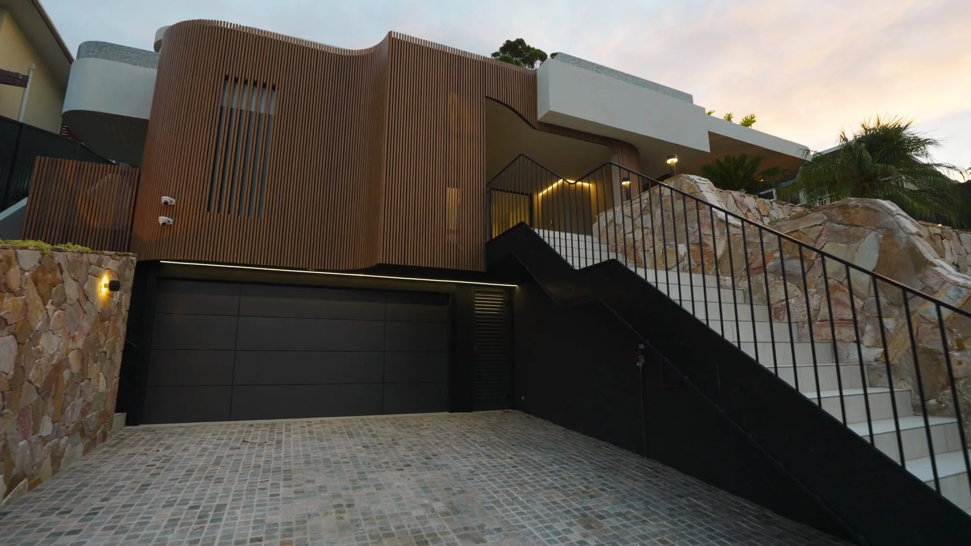 The 16 Sherwood Avenue home at dusk, its curved timber-batten facade above a natural-stone base
