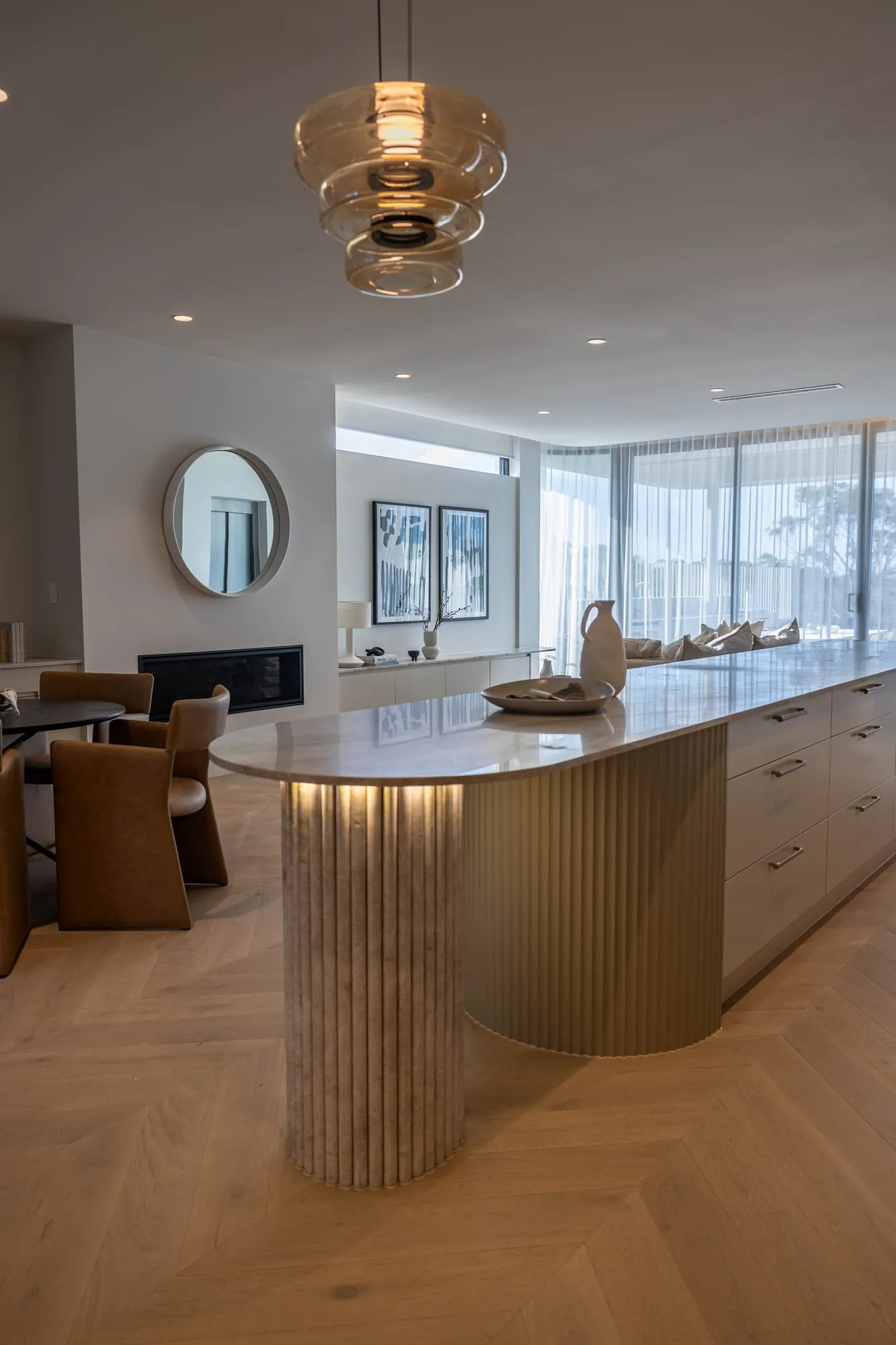Fluted stone island bench beneath sculptural pendants